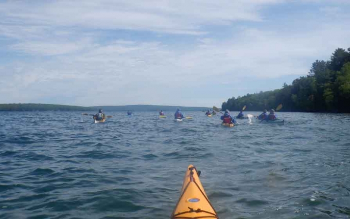 a group of kayaks are paddled on a blue lake with trees lining the shore